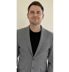 a man in a grey suit and black shirt is smiling for the camera