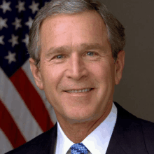 a man wearing a suit and tie smiles in front of an american flag