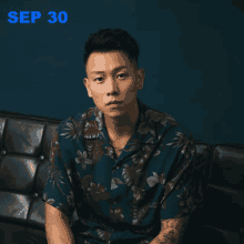 a man in a floral shirt sits on a couch in front of a blue wall with the date sep 30