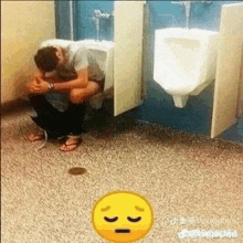 a man is sitting on a urinal in a public restroom .