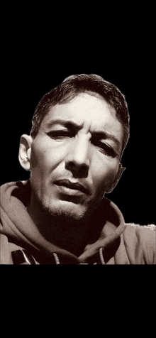 a man in a hoodie looks at the camera with a serious look on his face