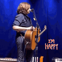 a man singing into a microphone while holding a guitar with the words " i 'm happy " on the bottom