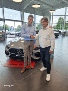 two men shaking hands in front of a car that says amg