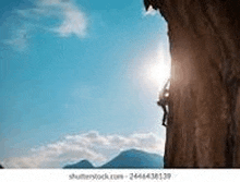 a person is climbing up a rock wall with the sun shining through it .