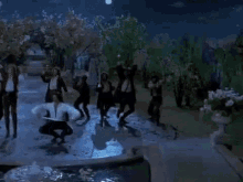 a group of people are dancing in front of a fountain in a garden .