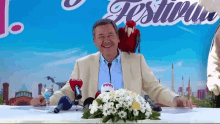 a man sitting at a table with flowers and microphones in front of a sign that says ' festival '