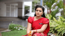 a woman in a red saree is sitting on the grass in front of a building .