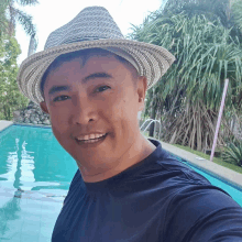 a man wearing a hat and a blue shirt smiles in front of a swimming pool