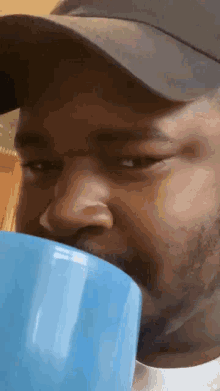 a man wearing a hat is drinking from a blue mug