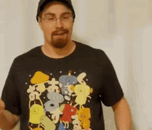 a man wearing a black t-shirt with cartoon characters on it is standing in front of a white wall .