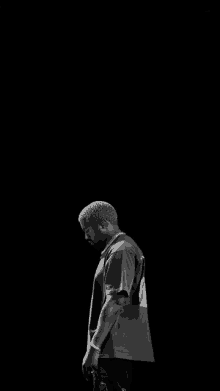 a black and white photo of a man in a t-shirt standing in front of a black background .