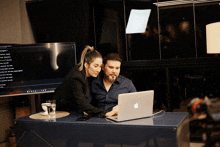 a man and woman looking at an apple laptop