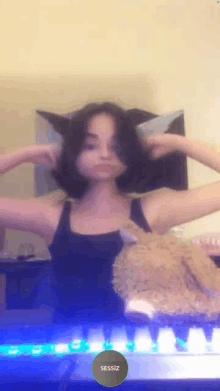 a girl in a black tank top with cat ears holds a teddy bear