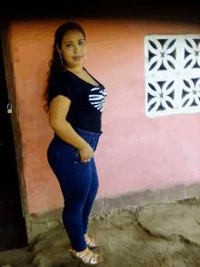 a woman standing in front of a pink wall wearing a black shirt