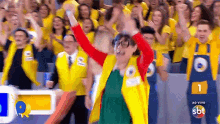 a woman in a yellow vest is standing in front of a crowd of people with their arms in the air .