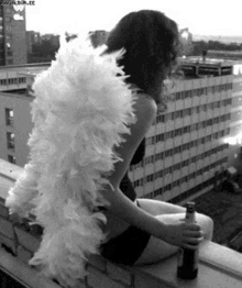 a woman with angel wings is sitting on a balcony holding a beer bottle .