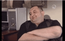 a man sits with his arms crossed in front of a computer monitor