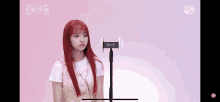 a girl with red hair is standing in front of a microphone with a pink background