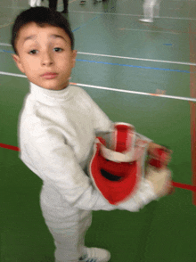 a young boy wearing a white shirt and white pants holds a red helmet