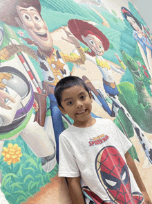 a boy wearing a spiderman shirt stands in front of a toy story wall mural