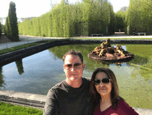 a man and a woman pose in front of a fountain