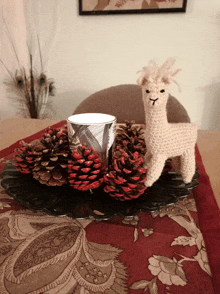 a crocheted llama sits on a plate of pine cones on a table