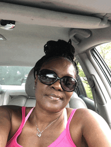 a woman wearing sunglasses and a pink tank top is smiling