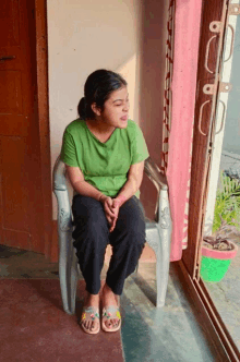 a woman in a green shirt sits in a chair looking out a window