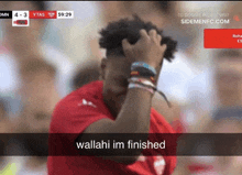 a man in a red shirt is covering his face while watching a soccer match