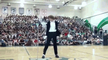 a man in a suit is dancing in front of a crowd in a gym with a banner that says stewart