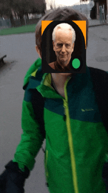 a man in a green jacket has a picture of an older man behind his face