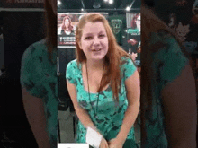 a woman with red hair is wearing a green shirt and talking to a camera .