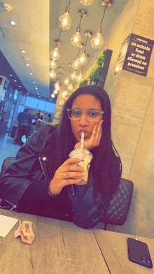 a woman sitting at a table with a drink in her hand and a sign that says no outside food or drink