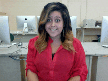 a woman in a red shirt is smiling in front of a computer