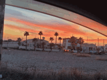 a sunset with palm trees and houses in the foreground