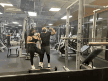 a man and a woman pose for a picture in a gym with a sign that says continue the burn to rack your weights