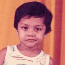 a young boy in a white tank top is looking at the camera .