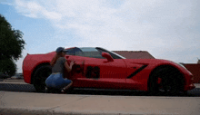 a woman is squatting down next to a red sports car with the word plan written on the side .