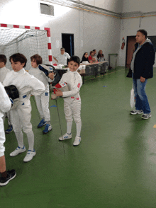 a group of young boys are playing fencing in a gym with a man standing in the background