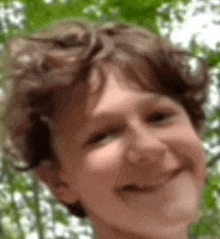 a close up of a young boy 's face with trees in the background smiling .