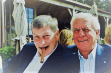 a man with a cigar in his mouth smiles next to another man