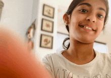 a young girl wearing a white shirt with the letter t on it smiles