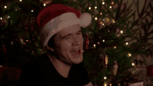 a man is wearing a santa hat in front of a christmas tree .