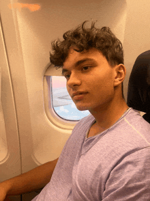 a young man in a purple shirt is sitting on an airplane looking out the window