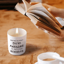 a person reading a book next to a candle that says you 're awesome so this is your reminder