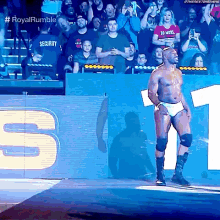 a wrestler is walking down the aisle with a crowd behind him and the words royal rumble on the screen behind him