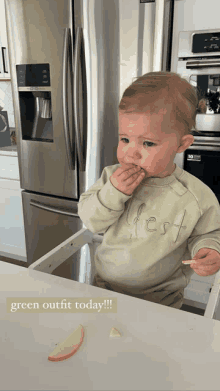 a baby wearing a green outfit is eating an apple slice