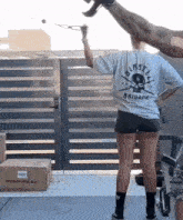 a woman wearing a t-shirt that says brigade is standing in front of a gate