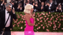 a woman in a pink dress is standing next to a man in a tuxedo on a red carpet .