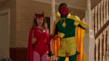 a woman in a red cape stands next to a man in a green cape holding a pumpkin